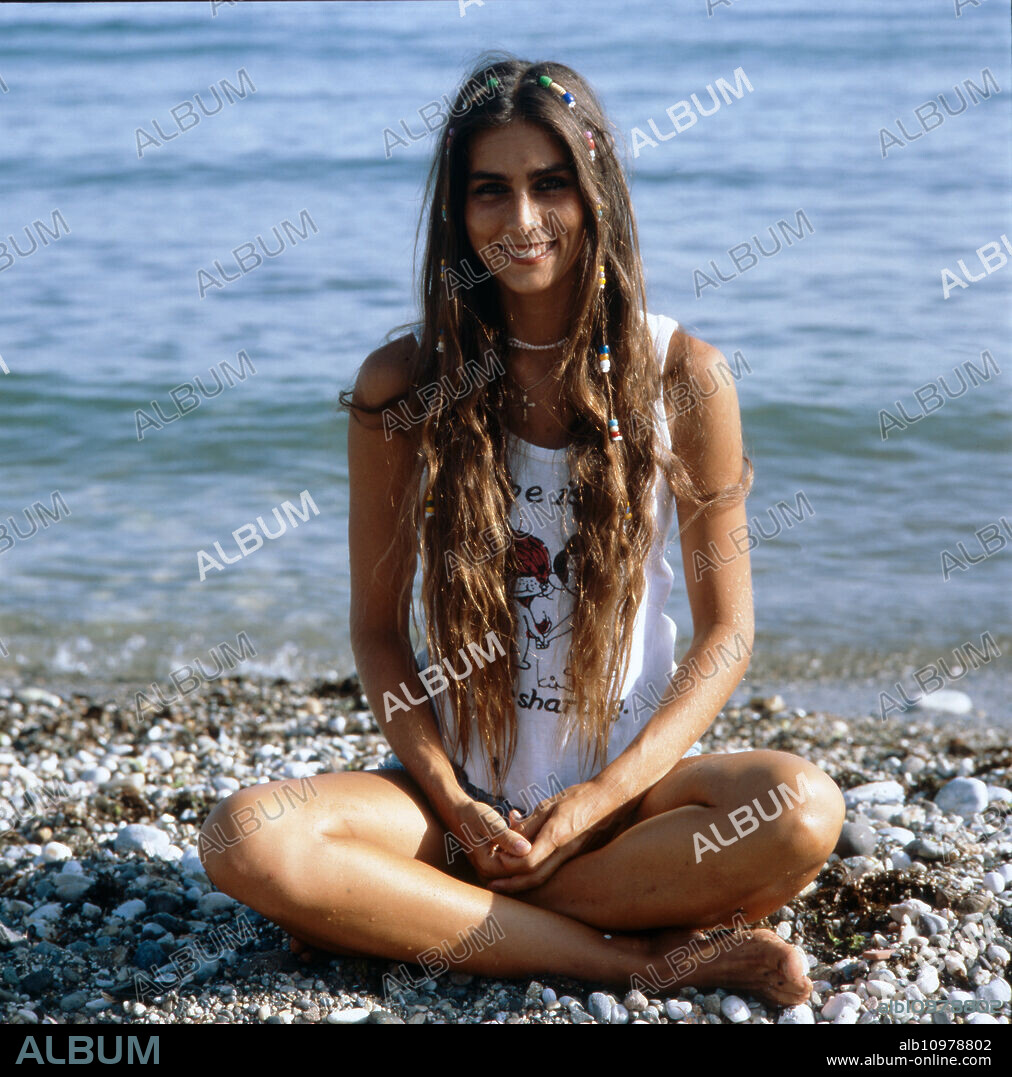 Home story of the Italian-American singer and actress Romina Power sitting cross-legged on the beach, Italy mid 1980s.