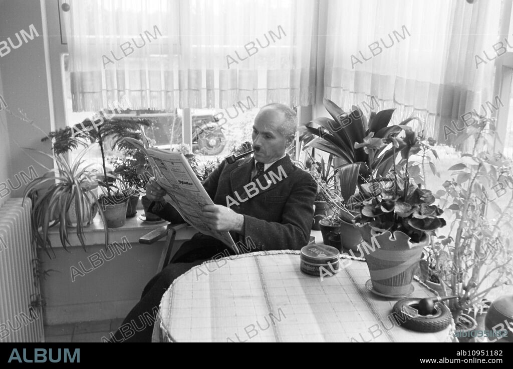 A man smoking a pipe and reading the Frankfurter Volksblatt in his winter garden in Zeppelinheim near Frankfurt am Main, Germany 1930s.