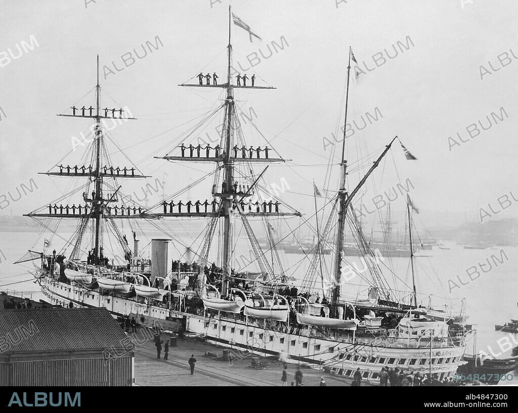Negative circa 1900, Victorian era. HMS Jumna in 1880, a Euphrates-class troopship launched at Palmers Shipbuilding and Iron Company in Hebburn on 24 September 1866. The shipâ€™s company are manning the rigging as the Royal Yacht Victoria and Albert comes a.
