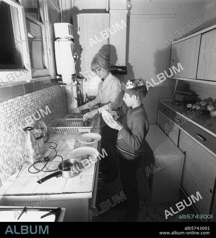 Travaux ménagers / Vaisselle. Dans la cuisine: la mère fait la vaisselle et  le fils l'essuie. Photo, France (entre 1948 et 1970). D'une série  Activités dans la cuisine. - Album alb5743001