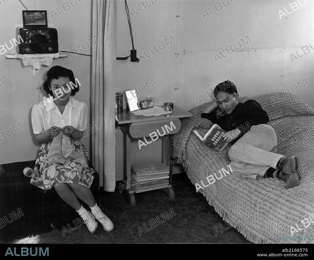 Mrs. Shimizu seated on couch with lacework, and Mr. Shimizu lying on bed, reading.  Ansel Easton Adams (1902 – 1984) was an American photographer, best known for his black-and-white photographs of the American West.  During part of his career, he was hired by the US Government to record life in the Japanese Internment Camp at Manzanar, California during WWII.
