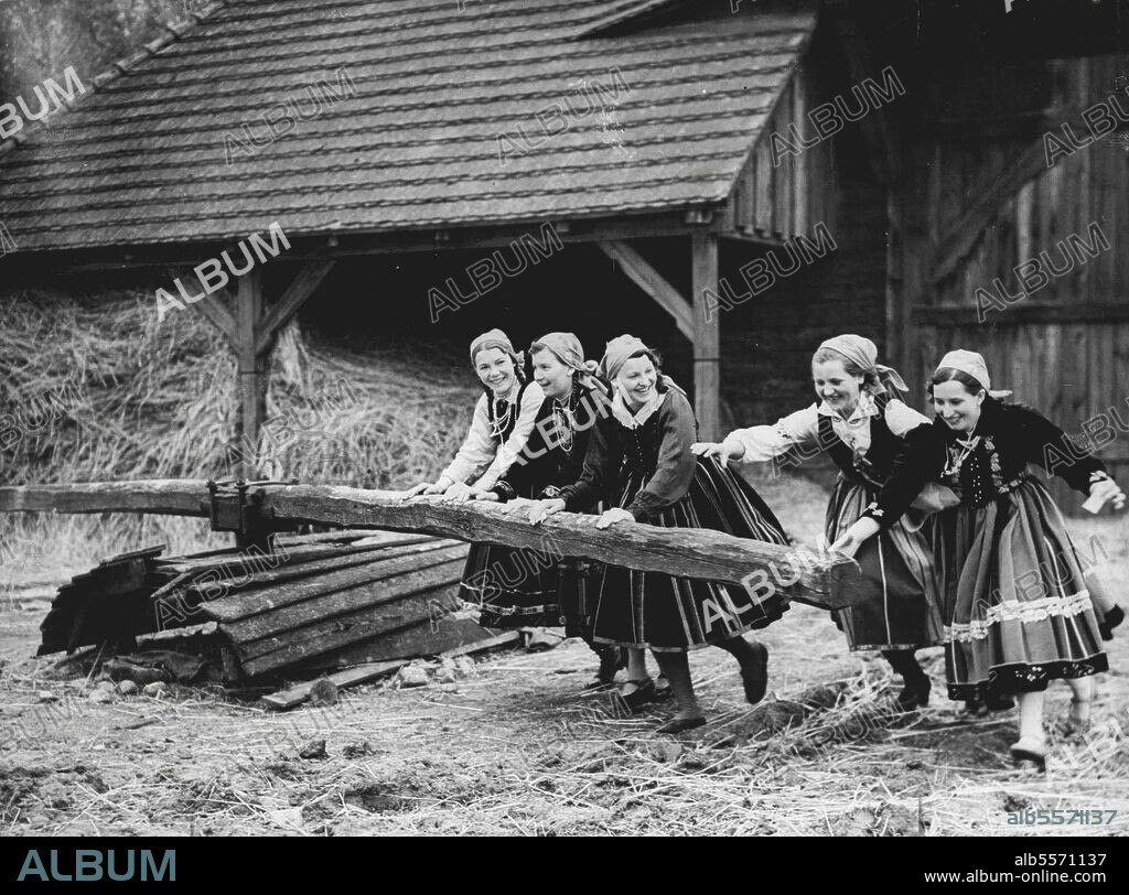 Poland's Women Will Tend The Land In Event Of War -- Polish girls, in national costume grinding corn with a primitive wheel on a farm near Lowicz. With the international situation still uncertain, Polish women are taking their dun precautions and are training as a land reserve in the event of war. The woman will take over work on the land while their menfolk are at the front. Compared with other European Powers, Poland is still largely agricultural. May 5, 1939.