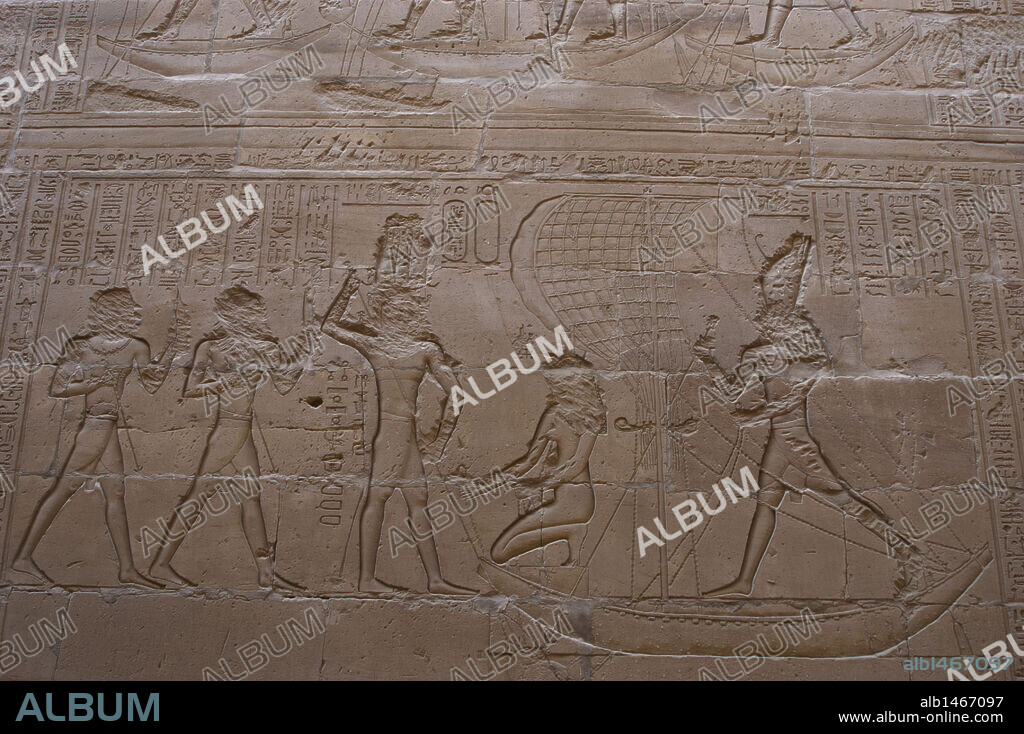 Arte Egipcio. Edfu. Templo de Horus. Siglo III A. C. Relieve que representa al dios Horus en batalla como venganza por el asesinato de su padre por su tio el dios Seth. Horus, de pie, e Isis, arrodillada, en un barco de vela capturando al hipopótamo (Seth). Todas las figuras tienen el rostro desfigurado.
