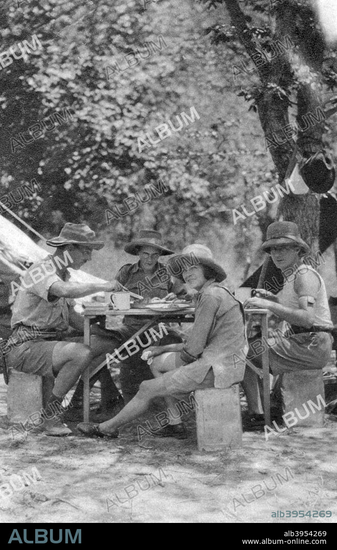 Meal time, Livingstone to Broken Hill, Northern Rhodesia, 1925 (1927). A print from Cape to Cairo, by Stella Court Treatt, George G Harrap & Company Ltd, 1927. The book was an account of the first successful journey by motor vehicle from Cape Town to Cairo, accomplished by Stella Court Treatt and her husband, Major Chaplin Court Treatt, in 1924-1926. This photograph shows expedition members Chaplin Court Treatt (1888-1954), Errol Hinds (1908-1980), Stella Court Treatt (1895-1976) and Thomas A Glover.