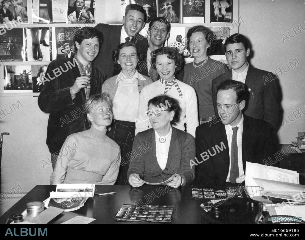 A young Ken Russell with colleagues - photo taken in Pictorial Press office, Salisbury Square House, EC4, c. March 1955. Standing (l-r) Ken Russell, John Jones (printer), Michael Holder (salesman), Ellen Hall (secretary), Philip ? (assistant printer, surname ?), Joyce Taylor (copy typist), Betty Fowler (photo librarian). Sitting (l-r) Cecelia Mitchell (in pink dress), Miss Kirby, David Mitchell. On wall behind at left: some shots from Ken Russell's Teddy Girl sequence. Picture probably taken by Tony Gale, late proprietor of Pictorial Press. ©TopFoto.