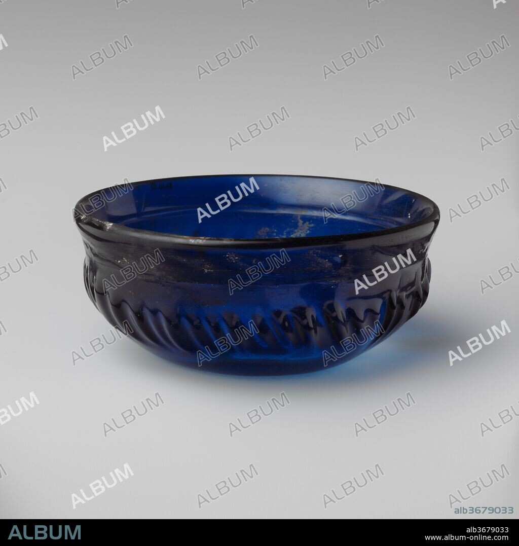 Glass ribbed bowl. Culture: Roman. Dimensions: H. 2 3/16 in. (5.6 cm); diameter  5 3/16 in. (13.2 cm). Date: first half of 1st century A.D..
Translucent cobalt blue.
Thick, slightly outsplayed rim with almost pointed edge, sloping inward below; convex curving side, tapering obliquely downward; concave bottom.
On interior, a single broad horizontal groove, cut at junction of rim and side; on exterior, forty-five short rounded ribs of varying width, thickness, and length.
Intact, except for minor chips in rim; some pinprick bubbles; faint dulling and iridescence, with small patches of encrusted weathering on interior.
Rotary grinding marks on interior and on band around exterior of rim; series of irregular tooling marks and indents on band around exterior of rim.