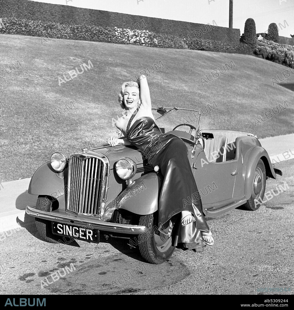 1953, Los Angeles, California, USA: American Actress model and singer MARILYN MONROE (Norma Jeane Mortenson) leans on a sports car and laughing while wearing her dress from the movie 'How to Marry a Millionaire.' Famous for playing comedic 'blonde bombshell' characters, she became one of the most popular sex symbols of the 1950s and early 1960s and was emblematic of the era's sexual revolution.