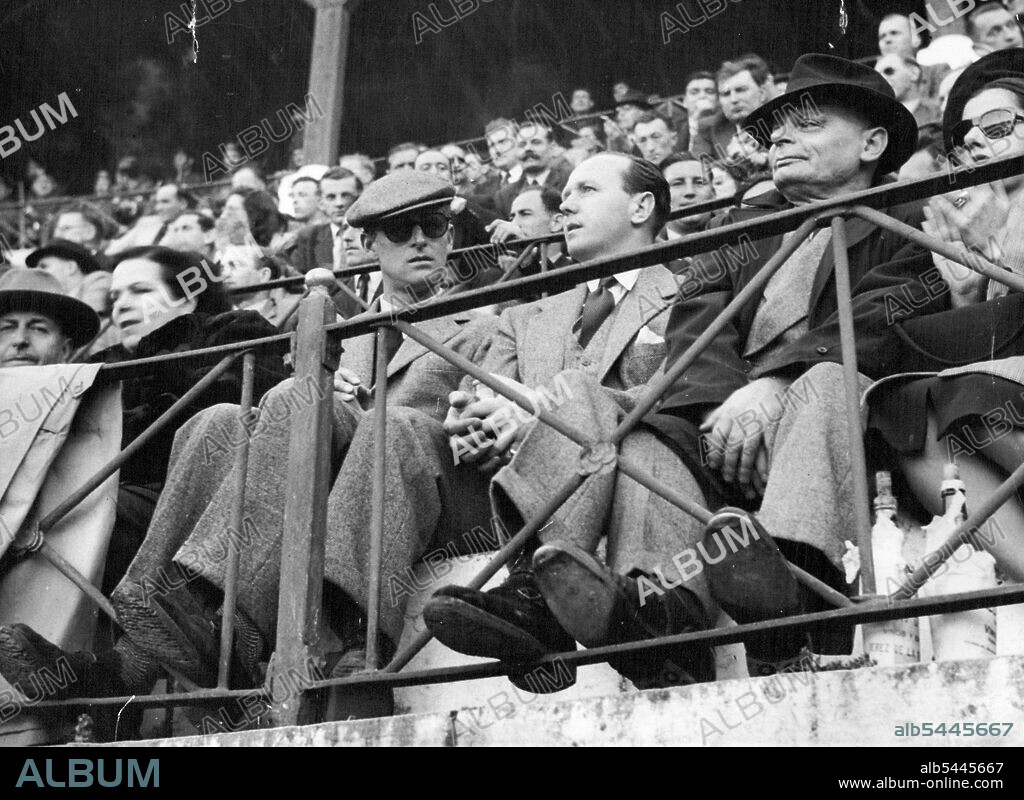 Bullfight -- Prince Philip in tweed suit and cap, is unrecognised in his dark glasses at the ringside. Next to him (right) is an unidentified friend. Unrecognised by the crowd, Prince Philip, Duke of Edinburgh, attended an out-of-season Bullfight in the local bullring at La Linea De La Conception, near Gibraltar, Feb , 25. The prince, in dark glasses and wearing a light green tweed suit with cap to match, sat in a ringside seat with an unidentified friend. The bullfights, reputedly for charity, cashed in on the presence of units of the British fleet which were in Gibraltar - the audience was predominantly British, Prince Philip, commander of the frigate HMS magpie, took some cine-photos of the second bullfight. March 30, 1951. (Photo by Associated Press Photo).