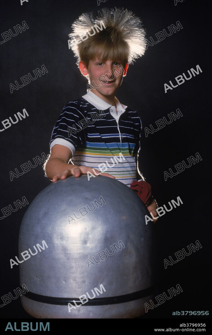 Static electricity. Male student with hair standing on end while touching a Van der Graaff generator. As the generator is charged, a static charge accumulates and leaks into the hair, migrating toward the ends. The charge is of one polarity, causing the hairs repel each other and to stand up.