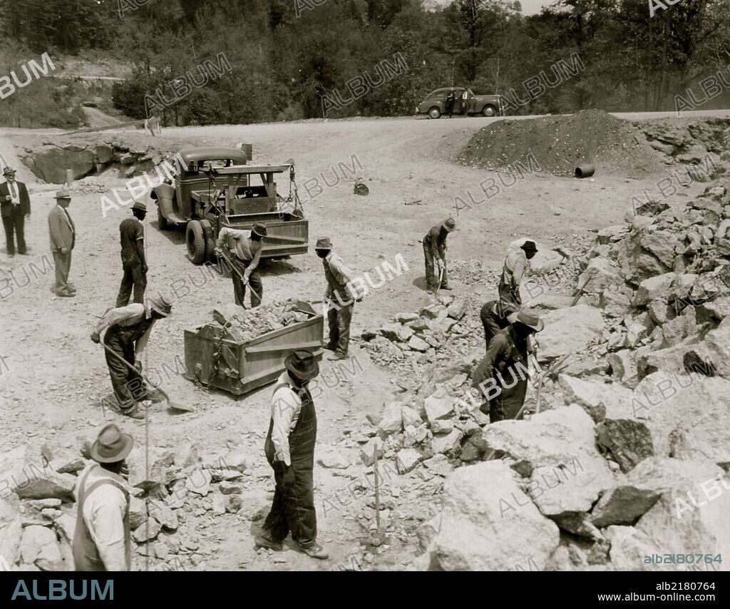 Prisoners breaking up rocks at a prison camp or road construction site.