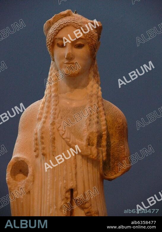HISTORIC VIEW OF THE OLD ACROPOLIS MUSEUM Kore Marble height:92 cm This kore is the work of an outstanding artist. view of the kore. She wears an chiton and a mantle falling from her shoulders in vertical folds. With a beautiful shaped face and the famous Archaic smile,a complex patterns of coiffure which ends in ringlets on her.