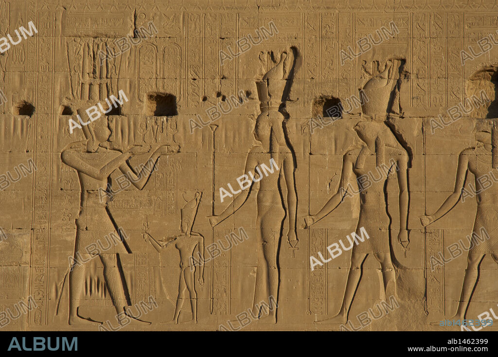 Egyptian Art. Dendera. Temple of Hathor. The god Ihy, as adult, making offerings before an small figure of Ihy, wearing a double crown and holds a sistrum in his hand, and gods Hathor (his mother) and Horus, both of them wearing a double crown too. Relief.
