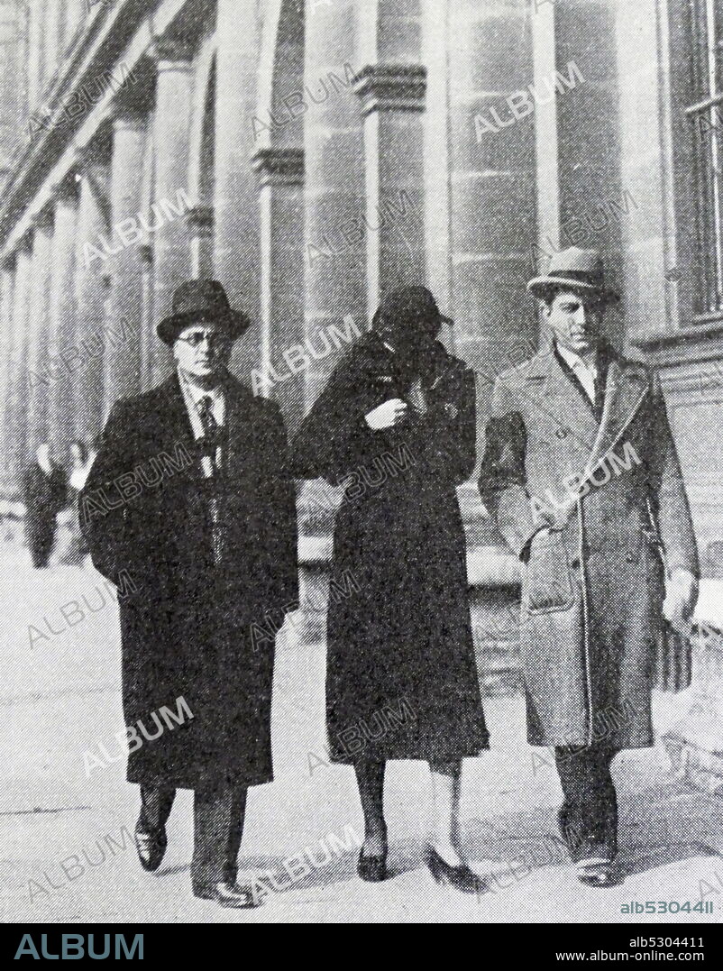 Black and white photo of Arlette Simon-Stavisky (1904-1988), wife of Alexandre Stavisky, walking down the street with two men and shielding her face from the cameraman.