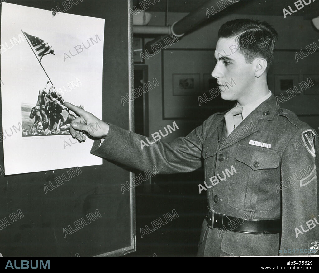 Marine Private First Class Rene Gagnon points to the figure of himself in the photos of Marines raising Old Glory atop Iwo Jima's Mount Suribachi. The picture will be used for the new 7th War Loan poster. 1945.