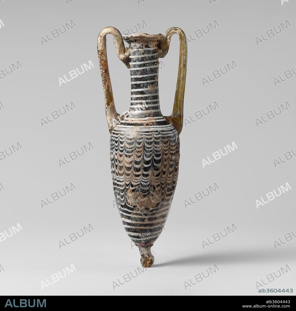 Glass amphoriskos (perfume bottle). Culture: Greek, Cypriot. Dimensions: 6 3/4 in. (17.1 cm)
Other: 1 15/16 in. (4.9 cm)
Diam. of rim: 1 1/16 in. (2.6 cm). Date: 1st century B.C..
Translucent green, appearing black; one handle and base-knob in yellow brown, the other handle in yellow green; trail in opaque white.
Inward-sloping rim-disk, with tooling indent underneath; tall, slightly concave, cylindrical neck; sloping shoulder; elongated piriform body; large applied base-knob; two rod handles applied in pads across shoulder, drawn up and slightly out to above rim, then looped in and down, and attached to neck below rim in a double fold over trail decoration.
Single white trail applied around lip of rim and then wound in a spiral around neck and shoulder to body, then tooled into a festoon pattern with twenty-eight upward strokes, continuing in a plain spiral around lower part of body, ending under base-knob.
Intact, except for part of knob; areas of deep pitting and dulling, with brilliant iridescence and creamy brown weathering.