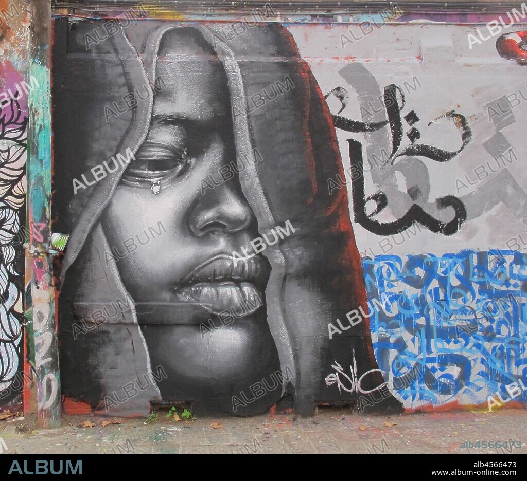 PIntura en grises de rostro de mujer llorando con capucha, graffiti mural, calle Selva de Mar, barrio Poblenou, Barcelona en 2016.