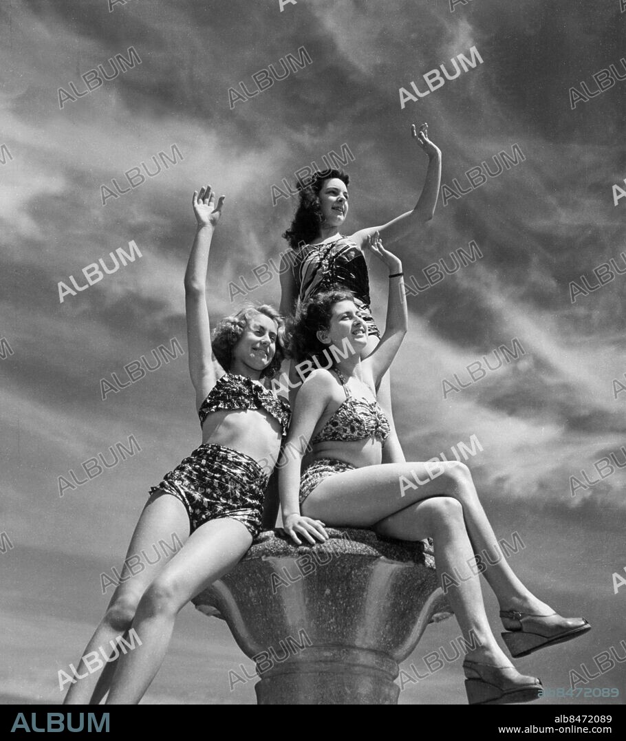 Orig. bildtext... GLAMOUR COMES TO THE SWIMMING POOL What do those glamorous girls we see gliding across the London stages do in their spare time? One answer to this was given at Enfiled Swimming Pool where three of the Windmill Lovelies spent a day in the sun. Wearing their new bathing costumes, they had a lot of fun and added charm and decoration. A decorative trio glamour to the skyline at the Enfield swimming pool. Windmill Lovelies Madeleine Hearne, Jean Weatherstone and Mavis Greenaway pose in their new swim suits during their day off at the pool. Anm. Baddräkter Bikinis Hälsningar Vinkningar Trio CD181 persons: Jean Weatherstone ;Madeleine Hearne ;Mavis Greenaway sites: STORBRITANNIEN.