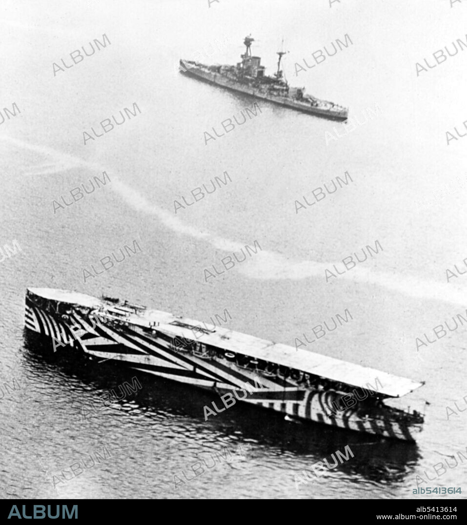 HMS Argus in British waters, 1918, an aircraft carrier that served in the Royal Navy and the first example of the standard pattern of aircraft carrier, with a full-length flight deck that allowed wheeled aircraft to take off and land. Dazzle camouflage was a family of ship camouflage used extensively in WWI. Credited to the British marine artist Norman Wilkinson it consisted of complex patterns of geometric shapes in contrasting colors, interrupting and intersecting each other. The intention of dazzle was not to conceal but to make it difficult to estimate a target's range, speed, and heading. (R class battleship is in the distance, cropped and cleaned).