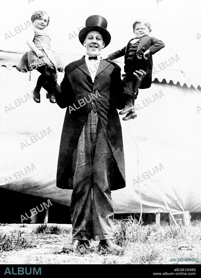 Entitled: "Johan Aassen holding a (unidentified) dwarf in each hand." John Aasen (March 5, 1890 - August 1, 1938) was an American silent film actor who was one of the tallest actors in history. In 1922, he was offered an acting job in a film called Why Worry? alongside the comedian Harold Lloyd. Later, he acted in several other films like Bengal Tiger, Charlie Chan at the Circus, Growing Pains, Should Married Men Go Home?, Legionnaires in Paris, Two Flaming Youths, The Sting of Stings, Long Fliv the King and the Tod Browning film Freaks, in a small uncredited cameo appearance. He died from pneumonia in 1938 at the age of 48. His body was later shipped to a doctor in Missouri for study and dissection. The skeleton was kept by the doctor, and eventually shipped to Loma Linda, California. According to the 1978 edition of Guinness World Records he was 7 feet tall. In June 2008, Loma Linda University confirmed that the 7 foot 2.4 inch skeleton they had in their collection was Aasen. Gigantism, also known as giantism, is a condition characterized by excessive growth and height significantly above average. In humans, this condition is caused by over-production of growth hormone in childhood resulting in people between 7 feet and 9 feet in height. Photographed by Al G. Barnes Amusement Company, 1923.