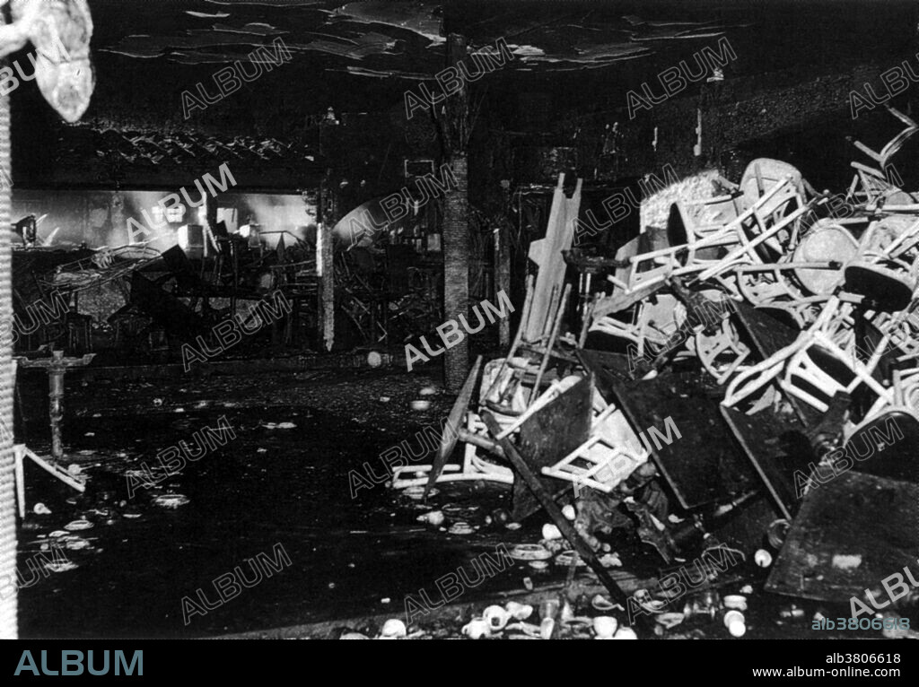 On November 28th 1942, a deadly fire occurred at the Cocoanut Grove Nightclub in Boston, Massachusetts, where 492 people perished. The club had a licensed capacity of 500 people, and on the night of the fire there were about 1000 people in the building. At about 10:15PM that evening, a busboy had been ordered to fix a light bulb, but needed to light a match to locate the light socket. Several patrons saw a flicker of a flame in the palm tree of the ceiling decorations. As other furnishings ignited, a fireball of flame and toxic gas raced across the room toward the stairs. The fireball traveled up the stairs and burst into the Foyer area, where coatrooms, restrooms and the main entrance were located. After a small number of people exited, the revolving door became jammed due to the crush of panicked patrons. Observers outside could only watch in horror as relatives and friends were crushed by the weight of the crowd surging against the jammed door. A view of the interior of the club after the fire.
