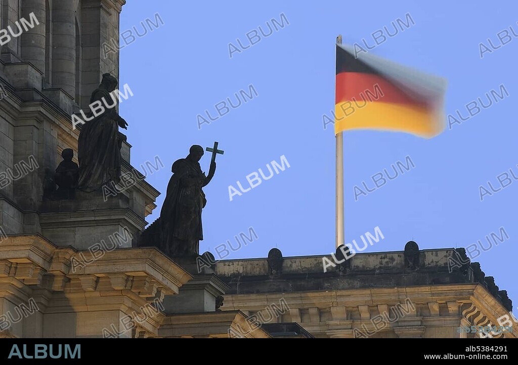 German flag waving on the roof of the Reichstag and a statue holding a cross (symbol for the Christian church), Berlin, Germany