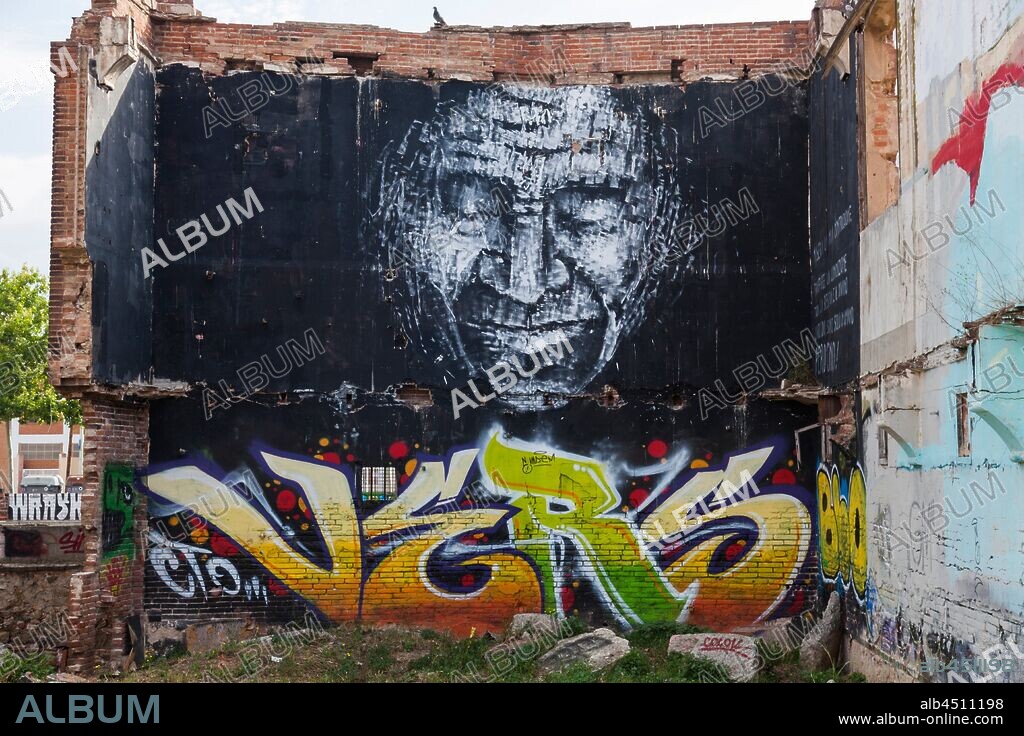 Pintura de rostro de hombre con ojos cerrados en tonos de grises sobre fondo negro y letras de colores debajo,graffiti mural, calle Venezuela, Poblenou, Distrito San Martin, Barcelona, en 2016.