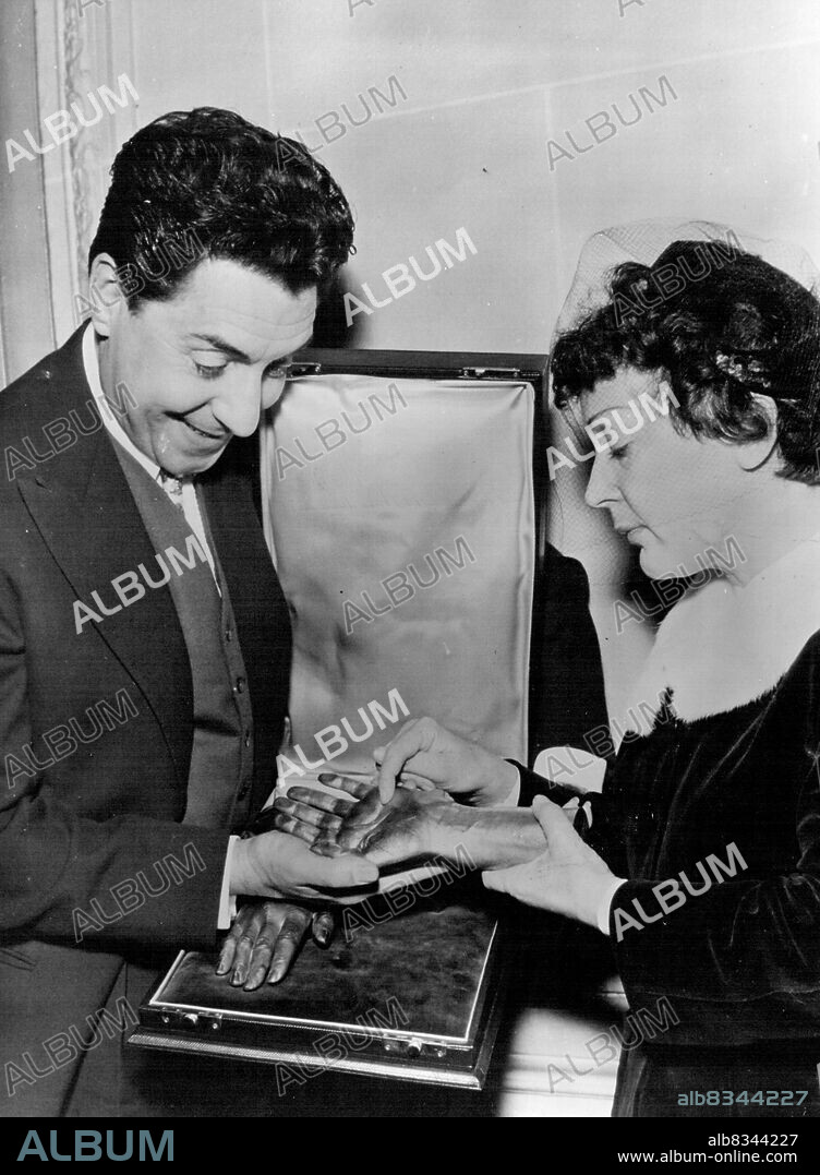 A Hand In Celebration -- Edith Piaf with husband Jacques Pills as they admire their unusual Anniversary gift. 
Singer Edith Piaf Celebrated Her first wedding anniversary in Paris yesterday.
At the Champs-Elysees Pavilion Edith was Presented a Bronze cast of her hands. 
The presentation was made by the her recording company. The Bronze hands were made by the Chiroteque Francais. January 5, 1954. (Photo by Paul Popper, Paul Popper Ltd.).