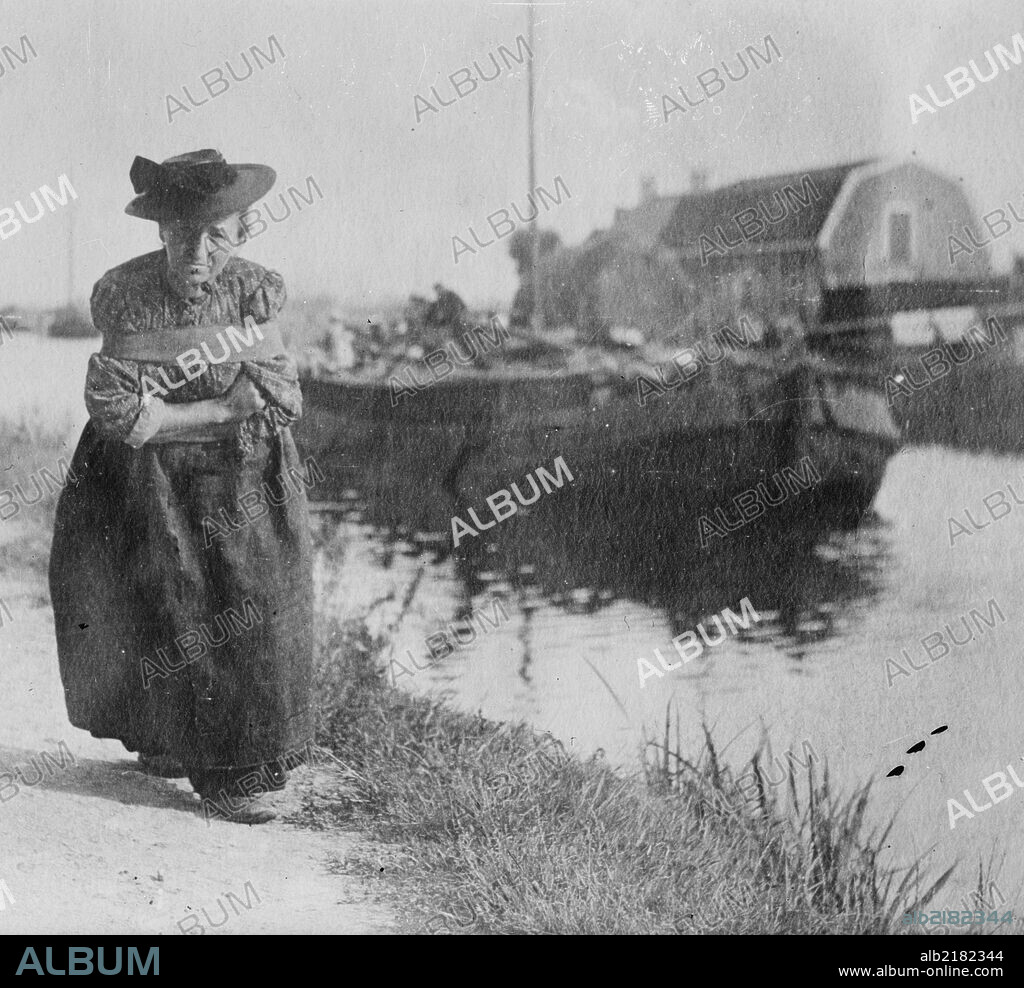 A Older Dutch woman has a bustle around her chest as she pulls a barge down a canal.