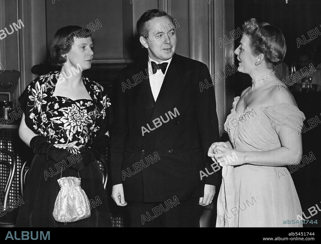 Gala Ballet At Royal Opera House, Covent Garden -- Mr. Harold Wilson, President of Board of Trade with his wife (left) wearing black dress decorated in silver, and Mrs. Digby Morton, in Moonshine Blue Edwardian dress.Buyers from all over the world arrive this week to see London fashion house's Spring collections. At the Royal Opera House. Covent Garden, this evening, the Incorporated Society of London Fashion Designers, entertained visitors. The Society have booked the Grand Tier for the evening ballet performance, and gave a supper party in the theatre. January 26, 1950. (Photo by Fox Photos).