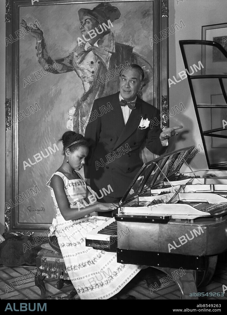 STOCKHOLM 1956-09-01. Karl Gerhard och adoptivdottern Fatima Gerhard tillsammans vid flygeln hemma i villan i Saltsjöbaden. Foto: TT Historical / kod 1900.