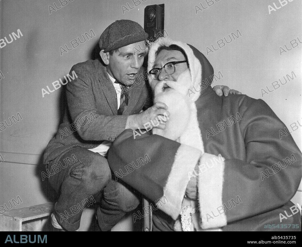 Gilbert As Father Christmas - Britain's comedian Norman Wisdom Whispers soothing words into Gilbert's ear. The role or Santa Claus is unusual for this fiery personality. Britain's television personality, Gilbert Harding, was Father Christmas for the Fitzroy Tavern Children's party which was held at the St. Pancras Town Hall, London. January 3, 1955. (Photo by Daily Express Picture).
