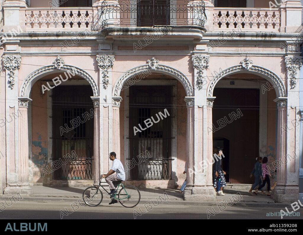A cyclist passing an ornate old building on Avenida Reina in central Havana, Cuba, West Indies, Central America.
