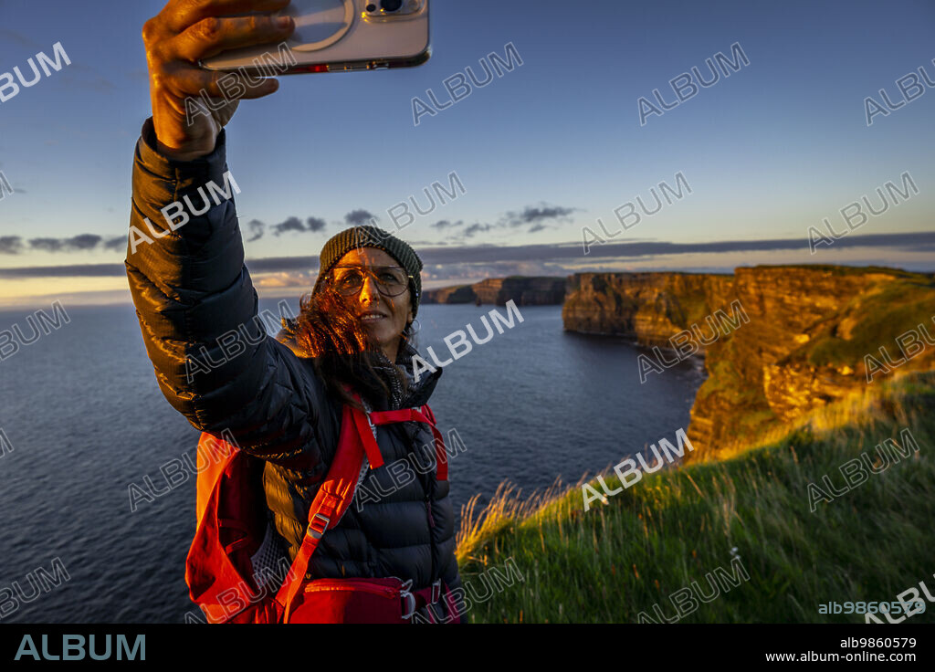 female hiker taking a selfie, Cliffs of Moher, The Burren, County Clare, Ireland, United Kingdom.