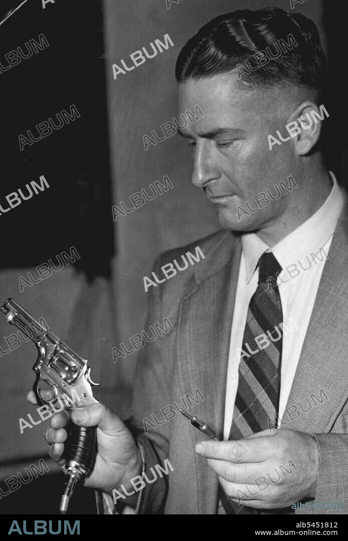 Police may ban this Swiss starting pistol from being used in the 1956 Olympic Games because of the Victorian Firearms Act. It is a prototype of the One used for the last two Olympics and was brought here to give. Australian officials experience in using it.But police took possession of it. The picture shows Snr. Constable McCully, of the Police Fire-arms office, inspecting the pistol. Same time It is specially designed with electric timing apparatus to start stop-watches a split second after the bang  the same time it takes for the noise to reach competitors. January 19, 1955.