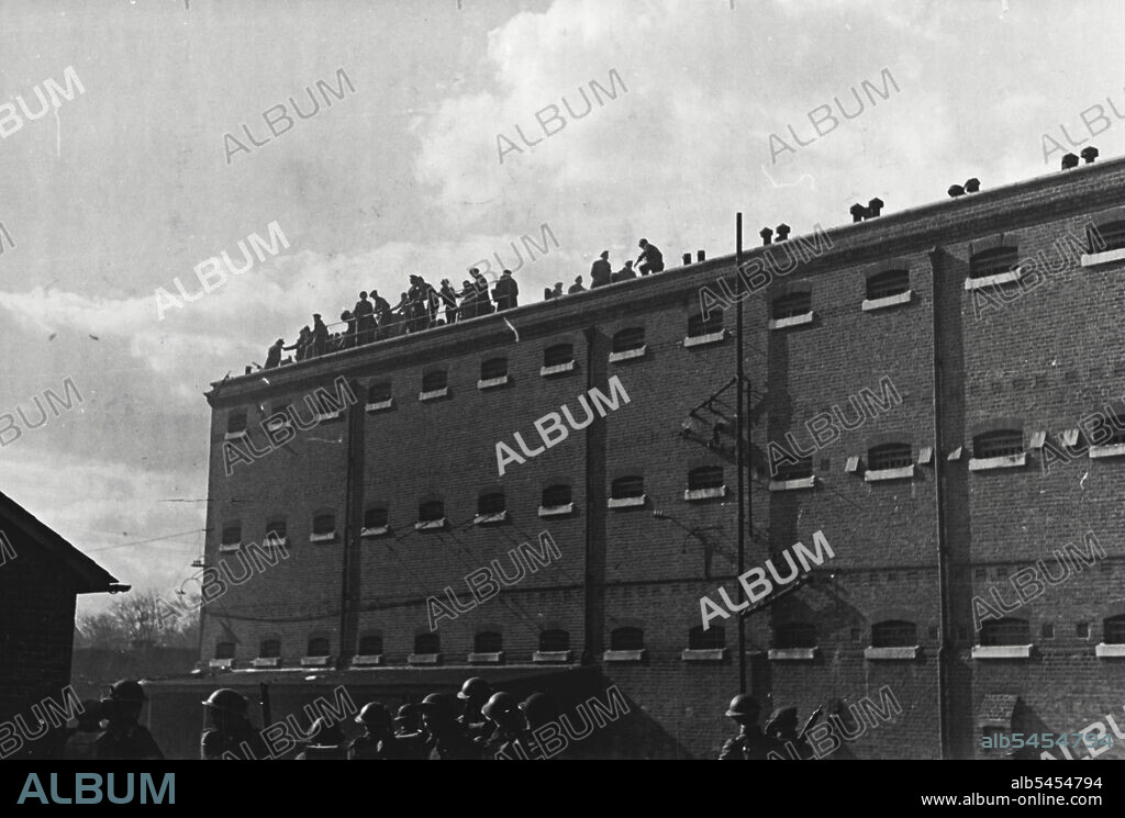 Wiggins Staff -- Prisoners on roof of Glasshouse. Tin hated soldiers stand guard in foreground. One hundred and fifty servicemen detained in the famous Aldershot Detention Barracks known as the "Glasshouse" rioted and completely wrecked their barracks over the weekend. February 24, 1946.
