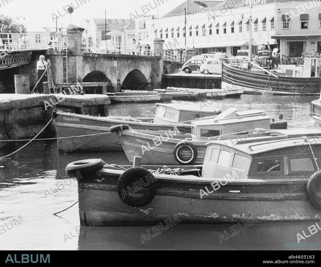 Barbados, The Careenage in Bridgetown. A number of small motor boats are moored along the Careenage. Bridgetown, Barbados, 1965.Caption reads 'THE CAREENAGE IS AN INLET OF THER SEA WHICH COMES RIGHT IN TO THE CITY ITSELF', 1965. 2005/010/1/13/28.