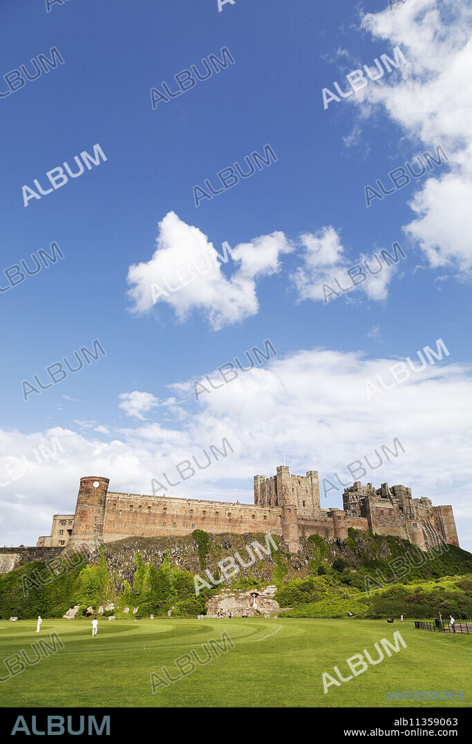 Bamburgh Castle, a medieval fortress, Grade I Listed Building constructed on top of a craggy outcrop of volcanic dolerite, overlooking a cricket ground, Bamburgh, Northumberland, England, United Kingdom, Europe.