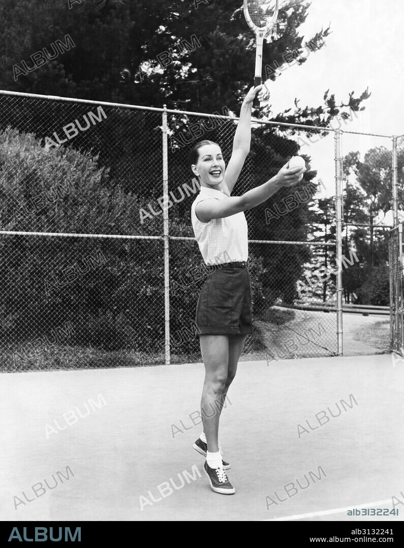 San Francisco, California:  June, 1953 Model Evelyn Frey prepares to serve with a smile in a tennis game advertisement for Joseph Magnin. She is wearing a checked cotton shirt, $4.95 and gabardine shorts, $3.95.