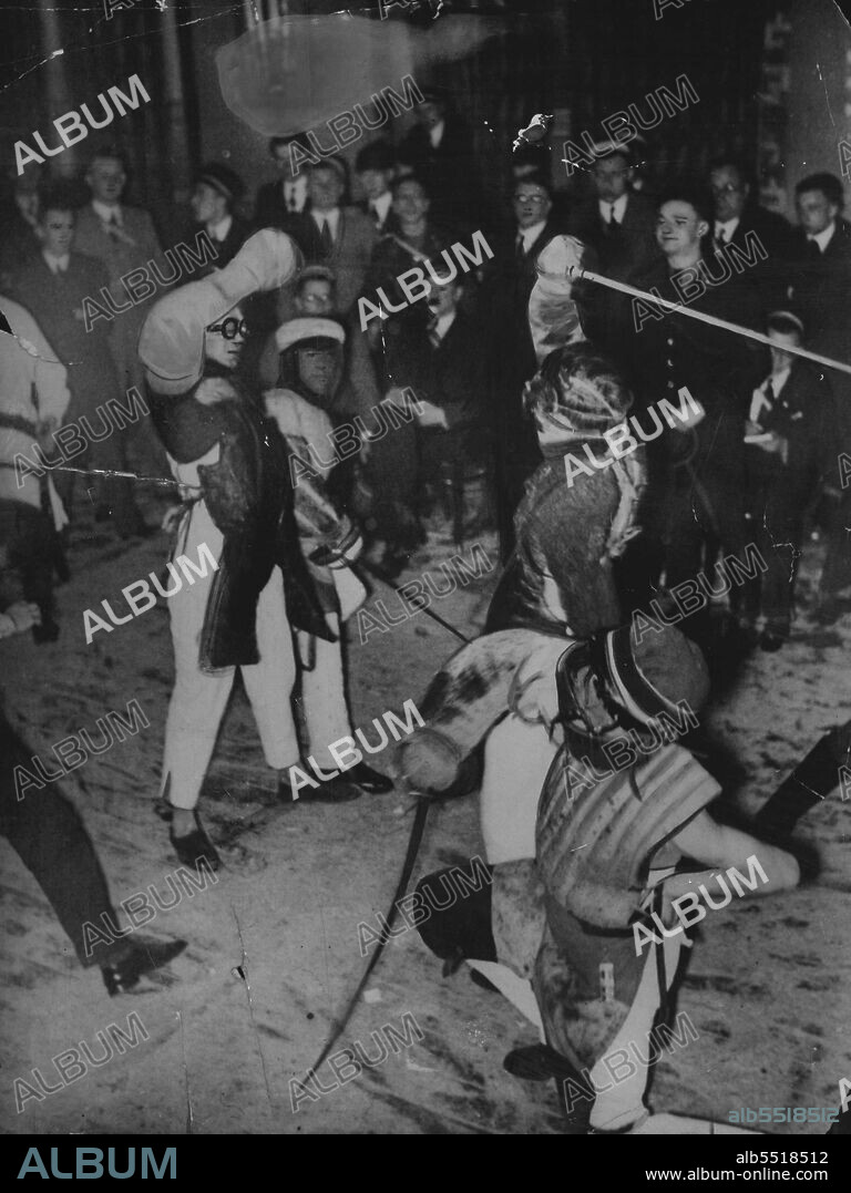Duelling Again in Germany - A "Mensur" duel in progress at a duelling club in Germany. The two seconds can be seen kneeling, holding their awards reads to intervene.Now that duelling is allowed again by law in Germany, in has become the favourite pastime of students, and duelling clubs have been formed all over the country. The most popular form of duel is the "Bensur", which consists of 40 passages of 40 passages of four hits each. As soon as four hits have been made, the seconds intervene with their swords and make the duellists break they.The duellists are well protected by wire-faced goggins, a thick bandage round the throat, and padded chest and right arm. He outsiders are allowed to witness these duels. April 01, 1934.