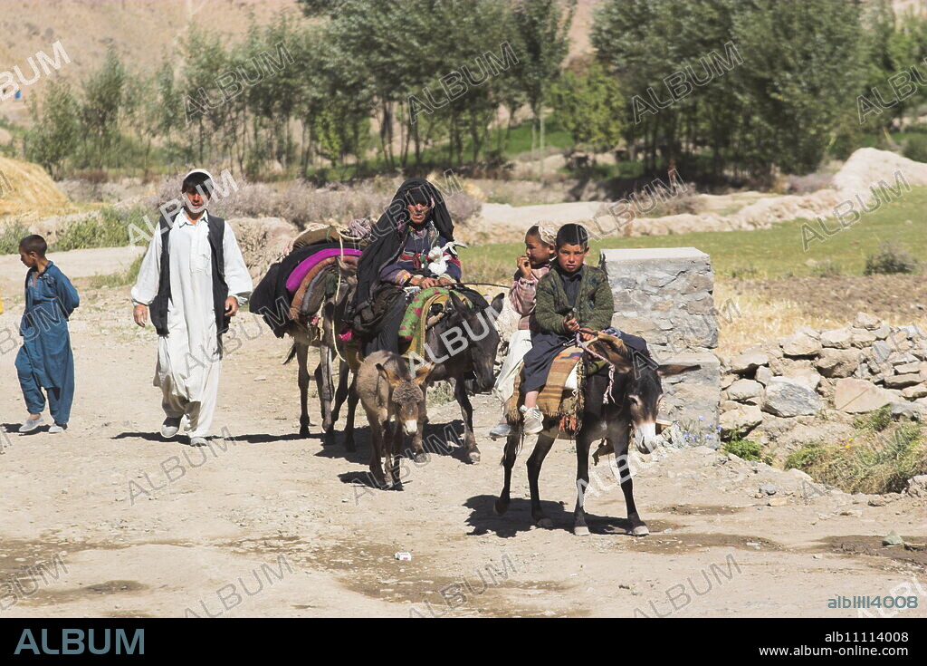 Aimaq people walking and riding donkeys entering village, Pal-Kotal-i-Guk, between Chakhcharan and Jam, Afghanistan, Asia.