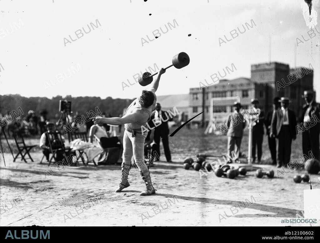 Athlete, weight lifting, standing on athletic field holding barbell, with one hand, over his head, 1904 Olympic Games.