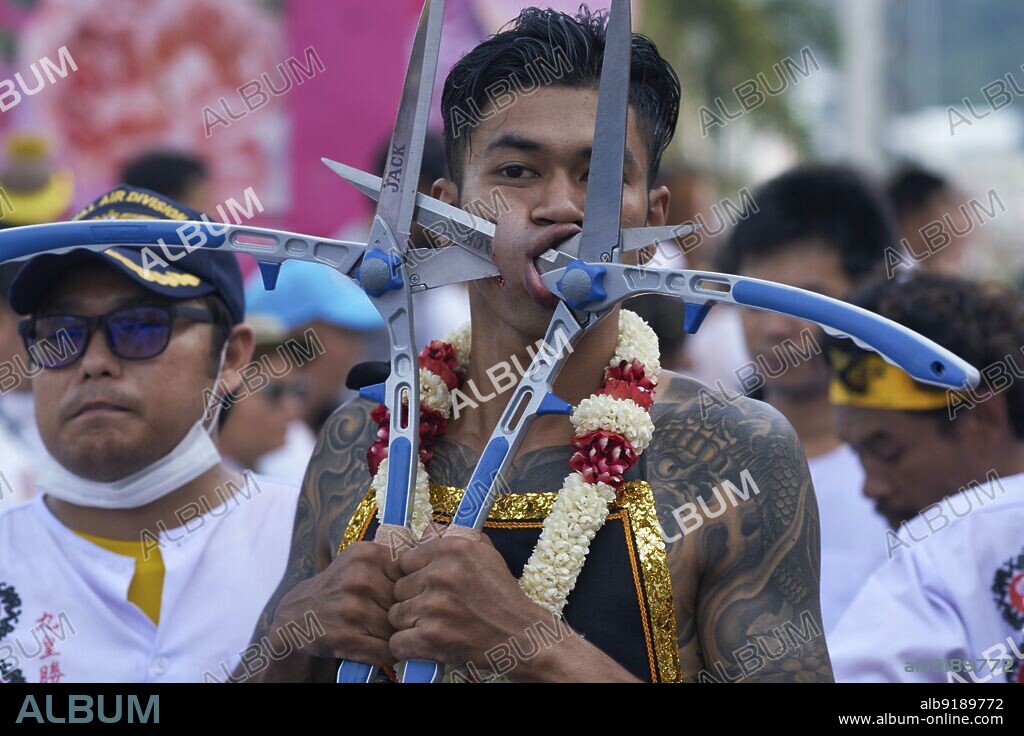 Thailand: A garlanded participant in a procession during the Vegetarian Festival in Phuket Town, a so-called Mah Song or spirit medium, his cheeks ritually pierced with garden scissors. The Vegetarian Festival is a religious festival annually held on the island of Phuket in southern Thailand. It attracts crowds of spectators because of many of the unusual religious rituals that are performed. Many religious devotees will slash themselves with swords, pierce their cheeks with sharp objects and commit other painful acts. The Nine Emperor Gods Festival is a nine-day Taoist celebration beginning on the eve of 9th lunar month of the Chinese calendar.