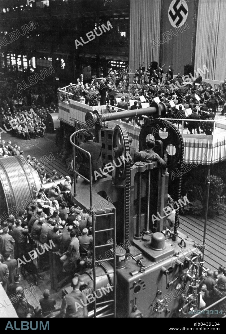 TYSKLAND BERLIN 1943-05-17. Orig. bildtext... FURTWÄNGLER DIRIGIERT IN EINEM BERLINER RUSTUNGSWERK. Das Reichspropagandaamt Berlin und der Oberbürgermeister der Reichshauptstadt veranstalteten heute in Verbindung mit der NS-Gemeinschaft "Kraft durch Freude" in einem grossen Berliner Rüstungswerk ein Werkkonzert mit den Wiener Philharmonikern unter Wilhelm Furtwängler. U.B.z. Furtwängler dirigiert. Blick in die Montagehalle. Foto: Weltbild / AB Text & Bilder / SVT / Kod: 5600 Mapp: Tyskland u.k: 1) Div. krigsindustri, 2) arbetare på fritid, under pauser o. dyl, samt 3) materialprovning. V 86:17 Bildserier Fotoreportage Åhörare Hakkors Dirigenter Fabriksarbetare persons: WILHELM FURTWÄNGLER sites: BERLIN;TYSKLAND.