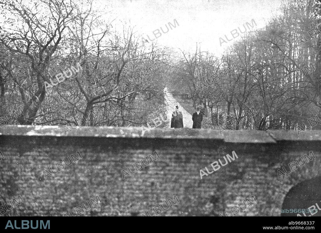 ''Dechu; Coiffe d'un chapeau tyrolien, une pelerine sur les epaules, l'ex-kaiser, accompagne par un des officiers qui l'ont suivi, le capitaine von Ilsermann, fait sa promenade matinale dans les allees du parc d'Amerongen clos de murs', 1918. From "L'Album de la Guerre 1914-1919, Volume 2" [L'Illustration, Paris, 1924].