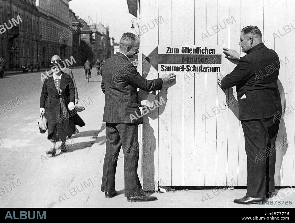 GERMANY BERLIN 1937-09-19. Orig. caption ... THE REICHSHAUPTSTADT ARMED FOR THE DARKLING EXERCISE. During the night from Sunday evening to Sunday and also on Sunday itself, the street scene of the Reich capital changed. Everywhere you look in the streets you can see the sidewalks of the street corners and the traffic hubs painted with white paint. Posters with indications of air-conditioning spaces are affixed to the houses and doors, indicating the number of persons accommodating them. U.B.z. the placement of plaques for the air protection cellar. Photo: Scherl Bilderdienst / AB Text & Bilder / SVT / Code: 5600 Folder: Civil Defense Germany Gas and air protection exercises 4057A Arrows Exercises for blackout sites: GERMANY; BERLIN.