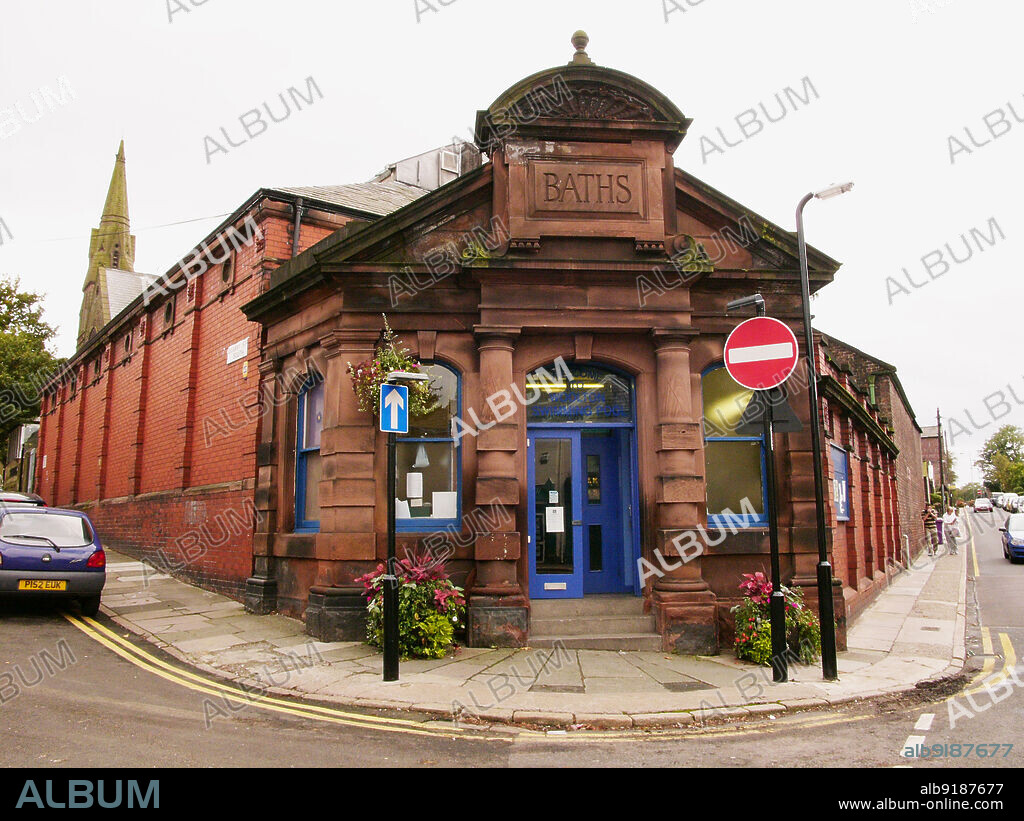 SIMON INGLIS. Woolton Baths, Quarry Street South, Woolton, Liverpool, 2006. The corner entrance of Woolton Baths, also known as Woolton Swimming Pool. The Woolton Baths, later known as the Woolton Swimming Pool, opened in 1893. The building was designed by the Manchester architects Horton & Bridgford, and funded by Holbrook Gaskell, a local philanthropist and chemical manufacturer. The entrance was designed in a Baroque Revival style and was constructed using local sandstone. The Woolton Baths closed to the public in 2010 and a campaign began to raise funds for repairs and restoration. They are a rare example of a small, late 19th century village swimming baths and are Grade II Listed.