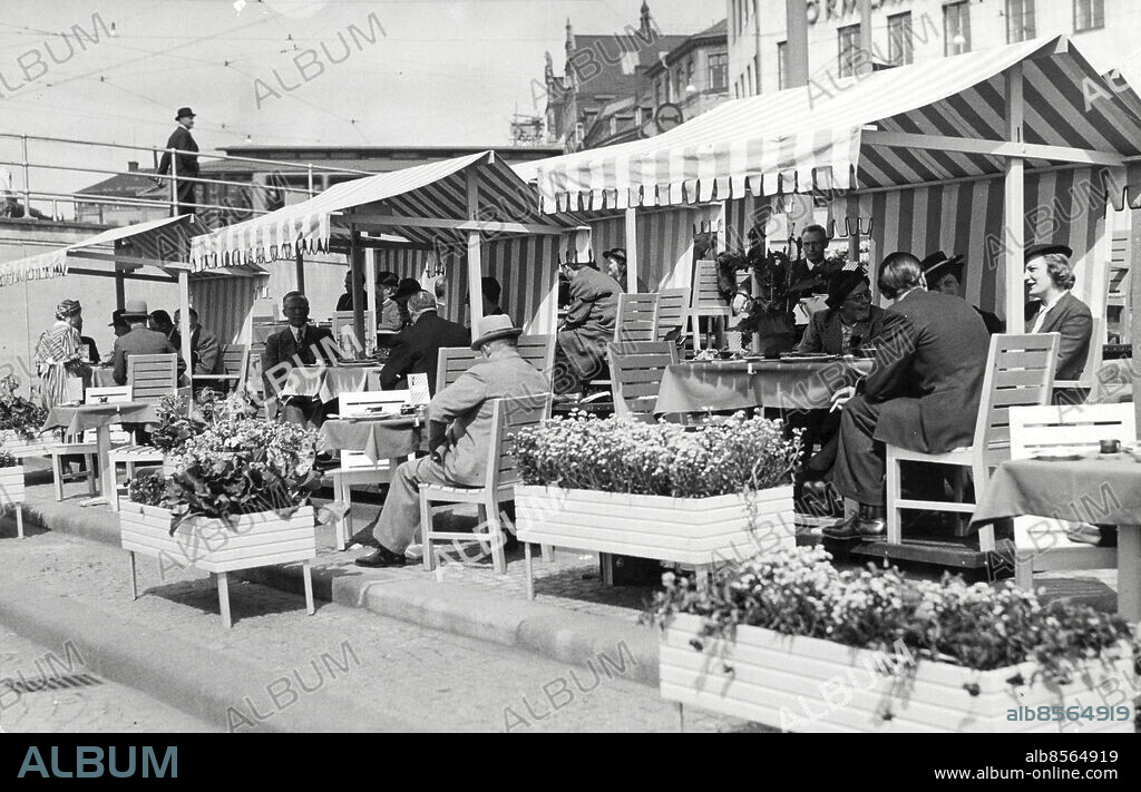 Stockholm 1938-05-19. Den nya serveringen vid Slussen.. På onsdagen öppnades ett våffelbruk på Slussen vid Karl XIV Johans staty. Det hela såg mycket glatt och trevligt ut med randiga uppasserskor, randig markiser och gröna och orangefärgade dukar. Borgarrådet Yngve Larsson, som efter vad innehavaren, direktör A Helin meddelade har äran av idén med en servering runtom ryttarstatyn, infann sig i arla morgonstund för att äta en invigningsvåffla.. Foto: DN / TT / Kod: 192. ** SvD OUT **.