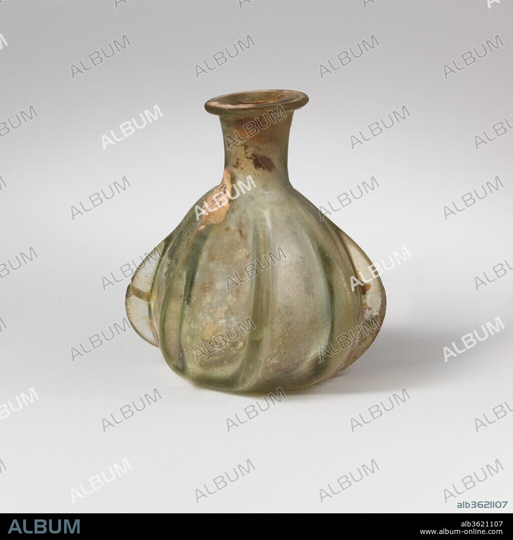 Glass ribbed bottle. Culture: Roman. Dimensions: H.: 2 1/4 in. (5.7 cm). Date: 1st century A.D..
Translucent light green.
Everted, horizontal rim; cylindrical, slightly funnel-shaped neck; squat piriform body; slightly concave bottom.
On body, seven irregularly spaced and shaped ribs with projecting rounded edges.
Intact, but one internal crack in body; some pinprick bubbles; patches of limy encrustation and creamy weathering, dulling, and iridescence.
Small, with heavy protruding ribs.