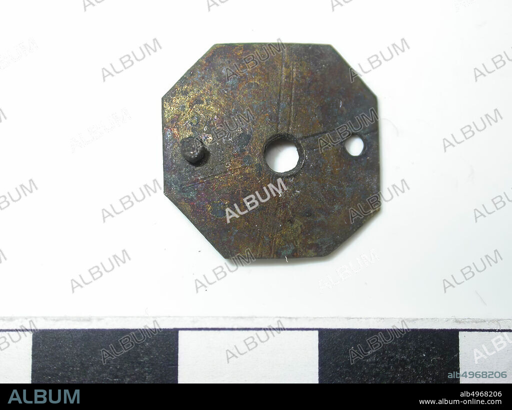 Octagon shape, gold (copper alloy). Octagon shape with a hole in the middle (diameter 0.1 cm). From the hole 2 lines run to the eight corners. Two pins were punched through the batter next to the hole. Back is hollow. 2 pin attachment, 1 pin missing. Pin is round. Length of the pin is 0.2 cm and the diameter is 0.1 cm, belt stroke, metal, copper alloy, Dm: 1.8 cm, D: 0.2 cm, end of the 14th century 1350-1400, Netherlands, Zeeland, Holly, Drowned Land.