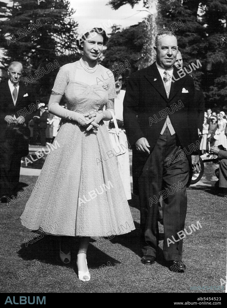 Queen Elizabeth with Mayor of Christchurch, Mr. R. M. MacFarlane, at the Civic Garden party in Civic Gardens Christchurch, NZ.Queen Elizabeth wore a full-skirted coffee coloured lace frock, white sling-back open toe shoes, close-fitting white hat, white gloves and handbag. January 29, 1954.